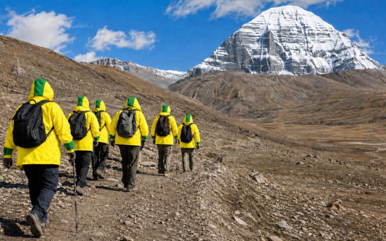 Rear-facing pilgrims wearing bright yellow jackets with thick green lower-forearm cuffs and two-tone hoods on the Mount Kailash parikrama trail
